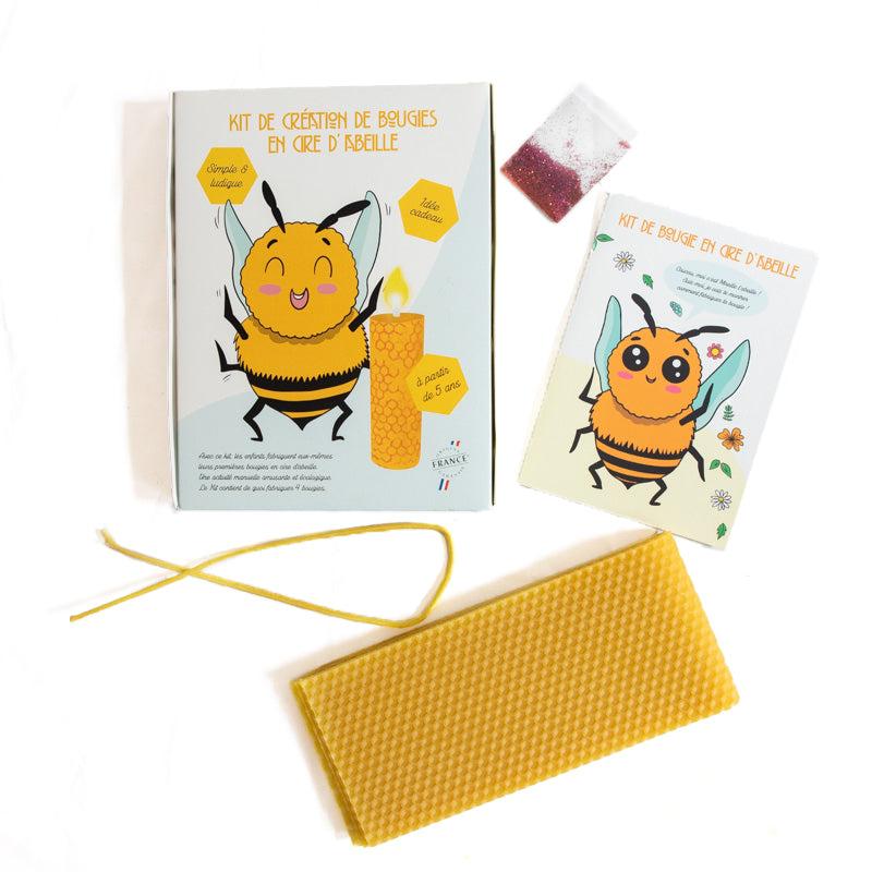 Vue complète du kit de fabrication de bougies pour enfants : boîte illustrée, livret pédagogique, plaque de cire gaufrée, mèche en coton et sachet de paillettes – La Fabrique de l’Abeille