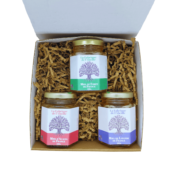 Coffret ouvert contenant trois pots de miel de France : miel de forêt, miel d’acacia et miel de lavande, sur lit de copeaux kraft, par La Fabrique de l’Abeille