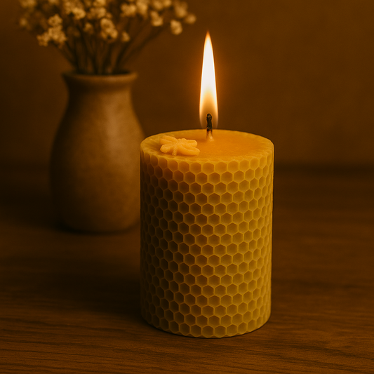 Photographie d'une bougie cylindrique en cire d'abeille naturelle, avec motif d'abeille visible sur le dessus, allumée dans un décor chaleureux et naturel, à côté d’un pot de fleurs séchées. Format 7 cm x 5,5 cm pour une durée de combustion d’environ 20 heures.