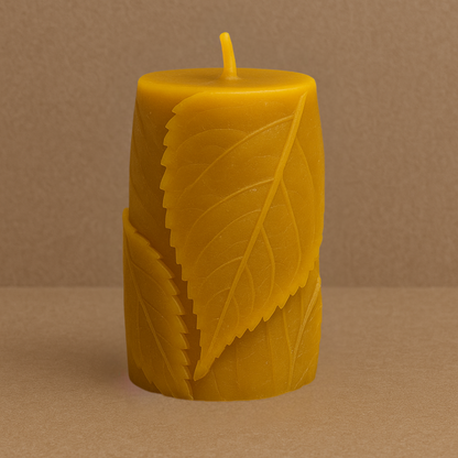 Bougie en cire d’abeille naturelle, sculptée avec des motifs de feuilles en relief, posée sur un fond marron uni. Format épais, idéale pour une combustion longue durée.