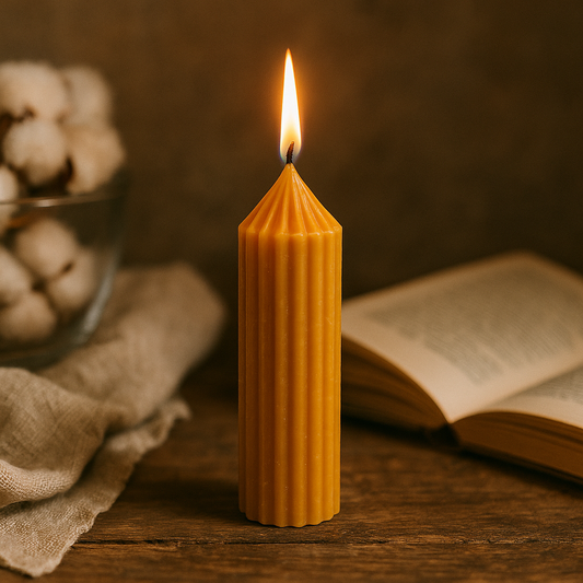  Bougie pilier M en cire d’abeille allumée, posée sur une table en bois avec un livre ouvert, un tissu en lin et un bol de coton, dans une ambiance naturelle et artisanale.