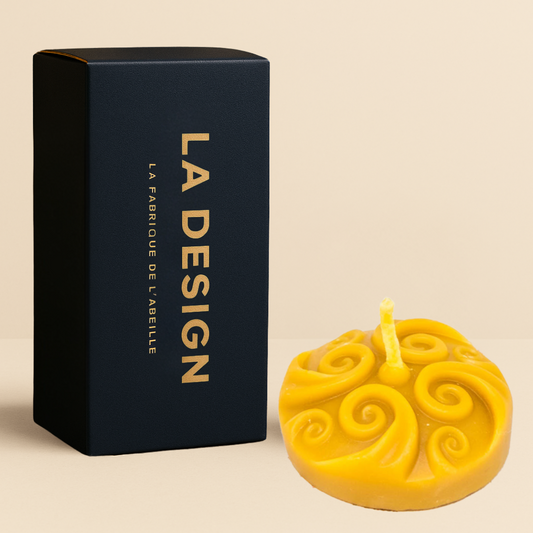 Bougie ronde en cire d'abeille avec motif sculpté en spirale, accompagnée de son packaging bleu marine "LA DESIGN" doré, posée sur fond beige.