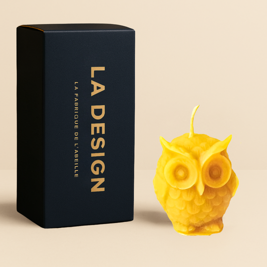 Bougie artisanale en cire d’abeille en forme de hibou, accompagnée de son packaging bleu marine "LA DESIGN" doré, posée sur un fond beige.