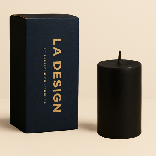 Bougie cylindrique noire accompagnée de son packaging bleu marine "LA DESIGN" avec dorure, posée sur un fond beige élégant.