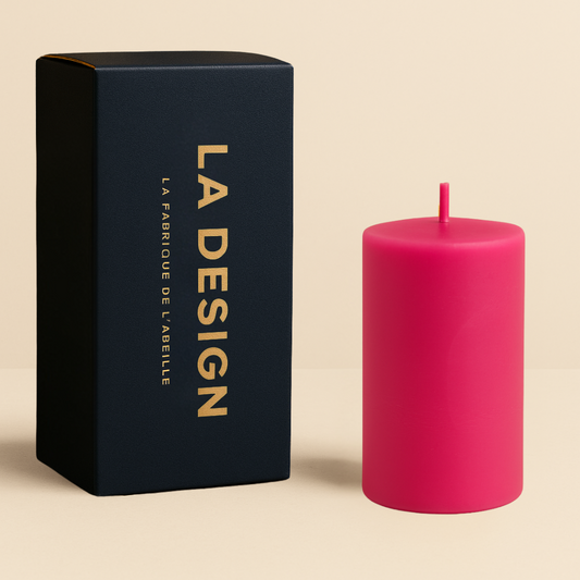 Bougie cylindrique rose avec packaging bleu marine et doré "LA DESIGN" de La Fabrique de l’Abeille, posée sur fond beige.
