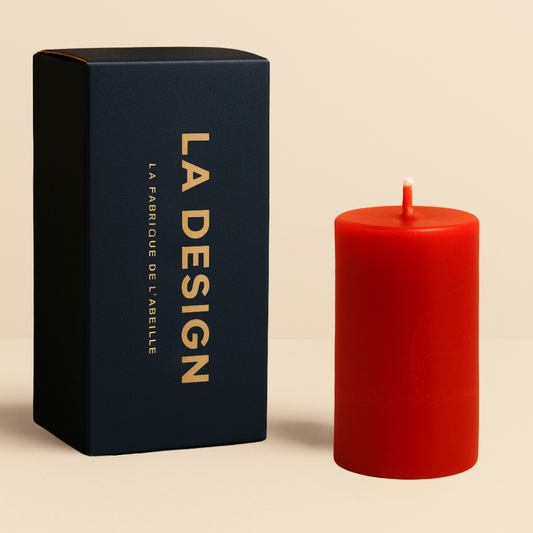 Bougie cylindrique rouge La Design avec packaging bleu marine et doré, posée sur fond beige doux.