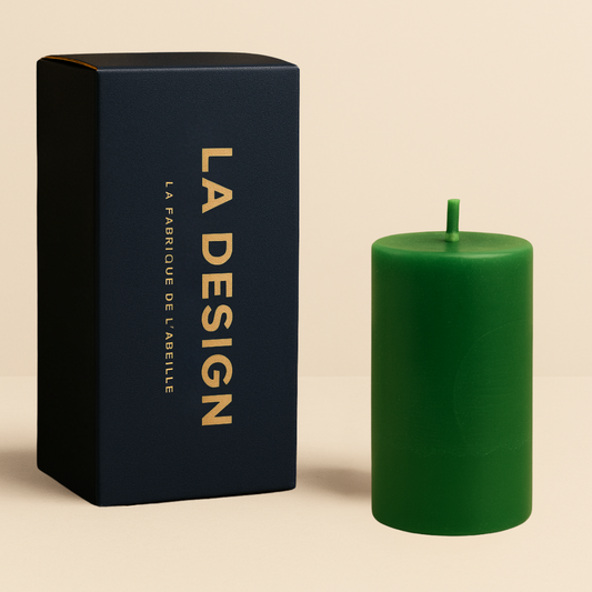 Bougie cylindrique verte accompagnée de son packaging bleu marine et doré "LA DESIGN", sur fond beige élégant.