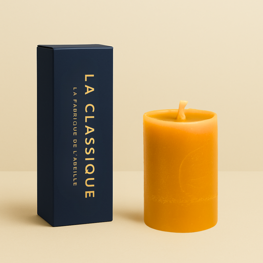  Bougie lissée en cire d'abeille, format 12h, avec packaging bleu marine "LA CLASSIQUE" doré, posée sur un fond beige.
