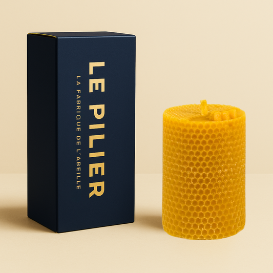 Bougie moulée en cire d'abeille au motif nid d’abeille, format 20h, accompagnée de son packaging bleu marine "LE PILIER" doré, posée sur fond beige.