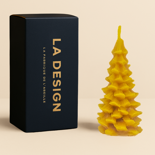 Bougie artisanale en forme de sapin en cire d'abeille, accompagnée de son packaging bleu marine "LA DESIGN" doré, posée sur fond beige.