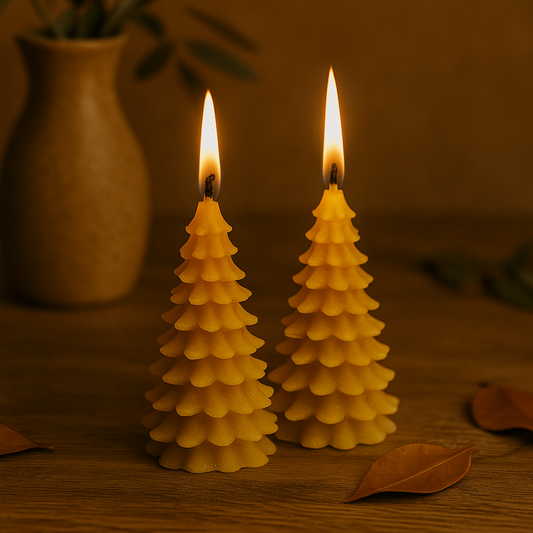 Deux bougies en forme de sapin de Noël en cire d’abeille naturelle, allumées, posées sur une surface chaleureuse, ambiance festive et artisanale.