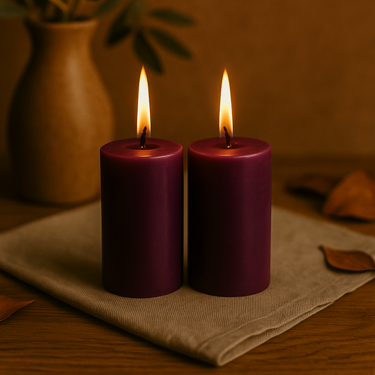 Deux bougies violettes allumées en cire d’abeille, de 7 cm de haut et 4 cm de large, posées sur une nappe beige, ambiance chaleureuse et automnale.