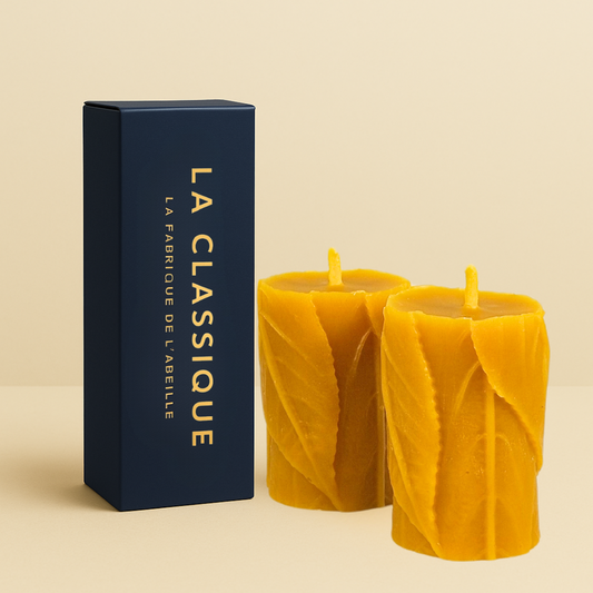 Paire de bougies artisanales en cire d’abeille avec motif feuille, accompagnées de leur packaging bleu marine "LA CLASSIQUE" doré, posées sur un fond beige.