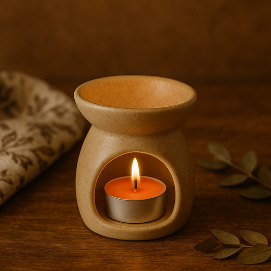 Chauffe-plat orange en cire d’abeille naturelle, allumé dans un brûle-parfum en céramique beige, sur une table en bois avec tissu fleuri et feuillage séché, ambiance artisanale et douce.