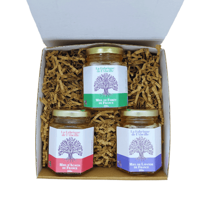 Coffret ouvert contenant trois pots de miel de France : miel de forêt, miel d’acacia et miel de lavande, sur lit de copeaux kraft, par La Fabrique de l’Abeille